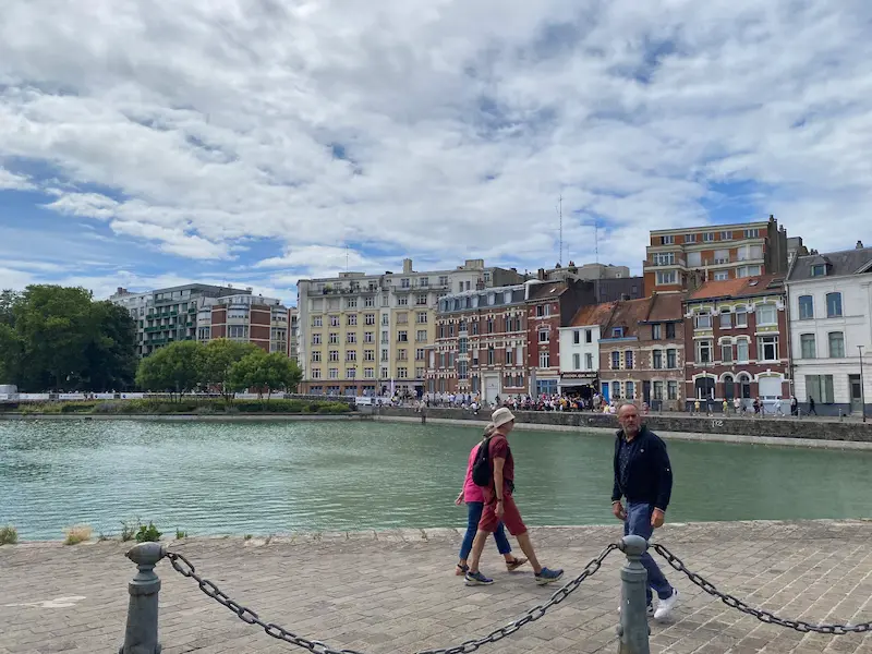 Quai du Wault in Lille, with historic waterfront buildings reflected in the water and pedestrians walking along the quayside.